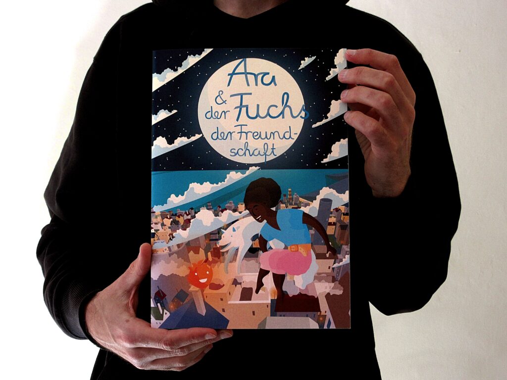 Eine Person in schwarzen Kapuzen-Pulli hält ein Heft im DIN-A4-Format hoch, auf dessen Cover ein über einer Stadt schwebendes, schwarzes Mädchen, ein weißer Fuchs und ein Feuer-Elementarwesen abgebildet sind.
