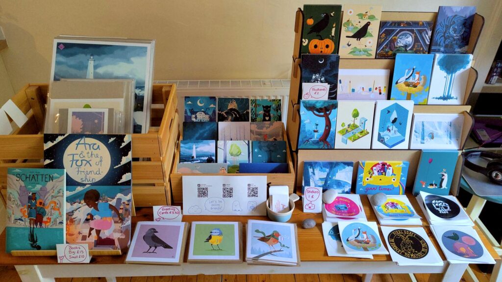 A table with all the things I'm going to sell: prints, comics, children's book, greeting and postcards and stickers.